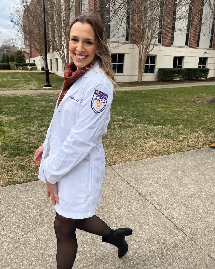 Woman wearing a white professional coat smiles as she walks outside.